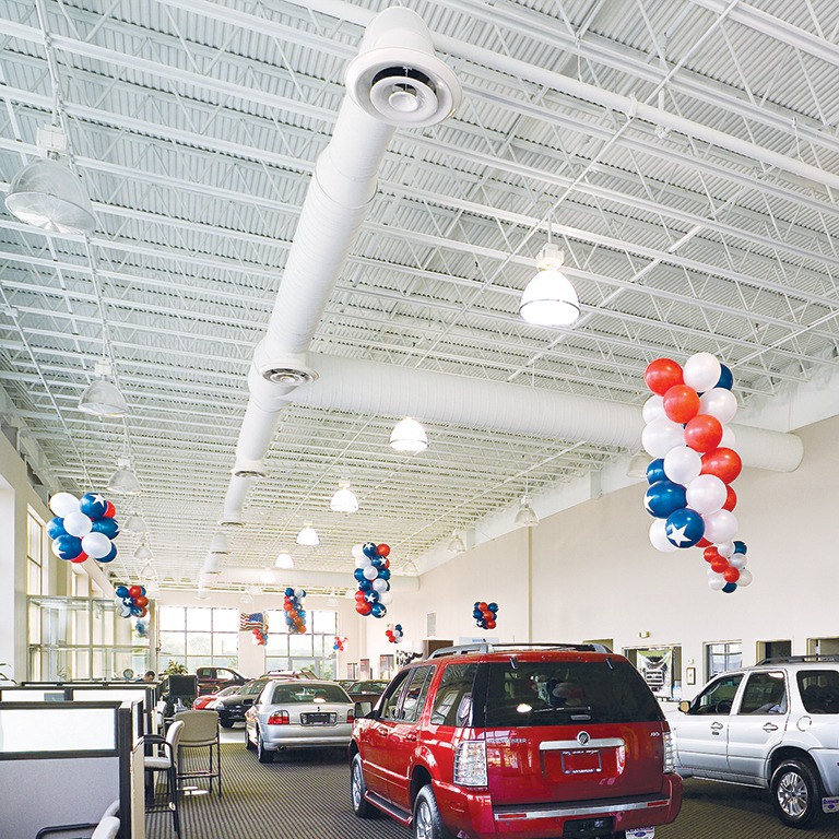 Interior of a car dealership showroom with multiple vehicles on display beneath a high white ceiling, decorated with red, white, and blue balloon columns.